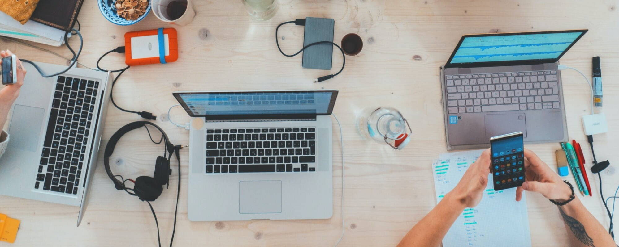 Laptops on a desk surrounded by headphones and chargers